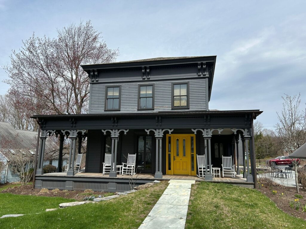 Prospect St. Writer's House, with gray and black trim and a yellow door, a large front port with white rockers.